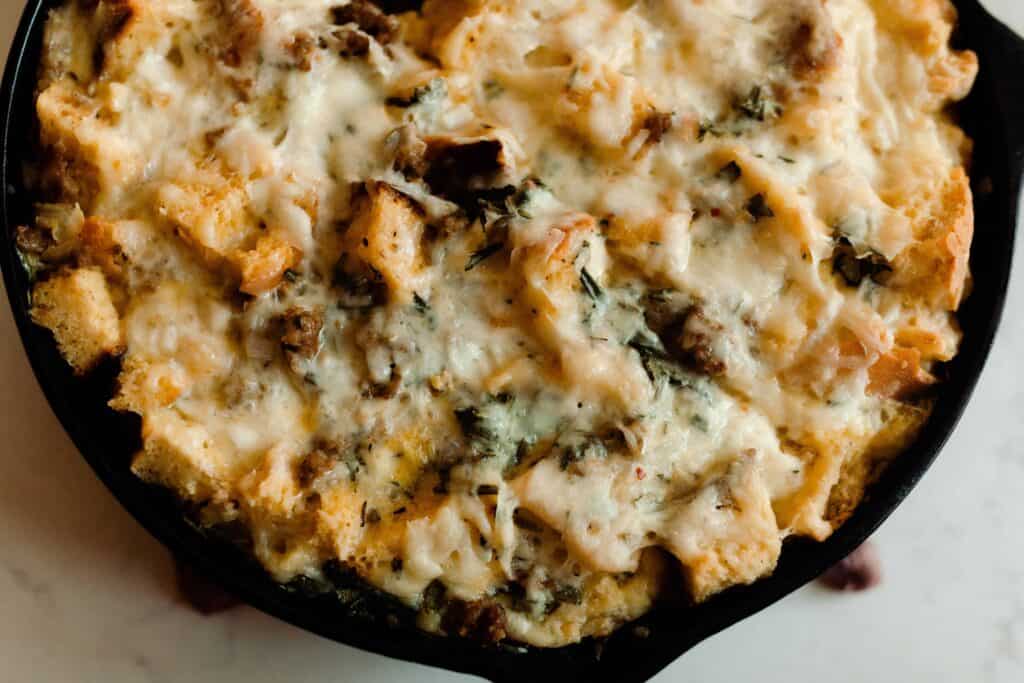 sourdough breakfast strata with sausage, cheese, and herbs in a cast iron skillet