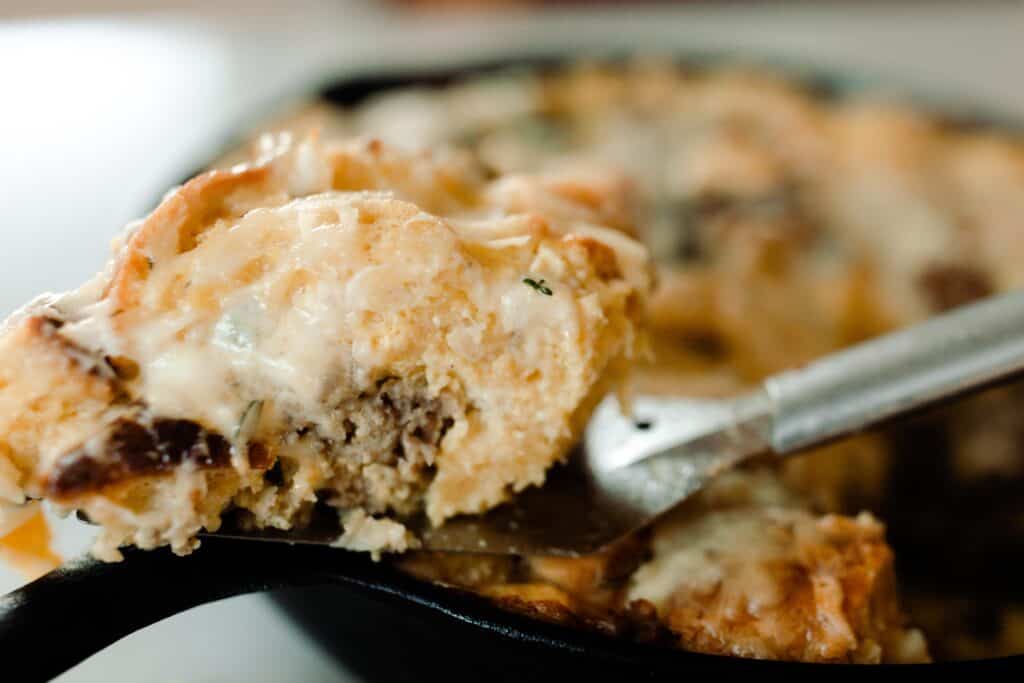 slice of breakfast strata on a serving spatula resting on a cast iron skillet