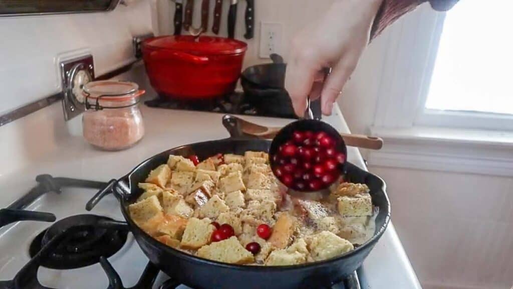 adding cranberries to the top of sourdough French toast casserole in a cast iron skillet