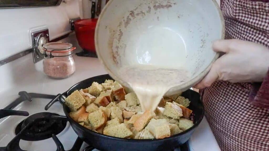 pouring custard over sourdough bread in a cast iron skillet