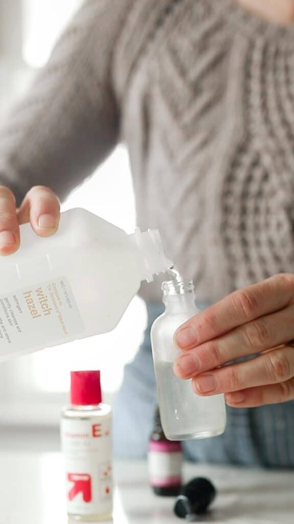 women wearing a tan cable knit sweater pouring witch hazel into a jar