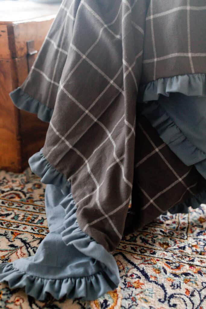 plaid and blue double sided flannel blanket with ruffles drapped over a chair wit