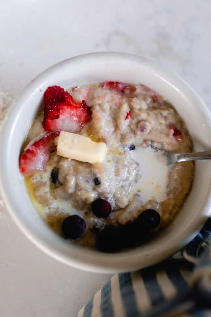 overhead photo of a bowl of einkorn cream of wheat with strawberries, blueberries, and a pat of butter in a white bowl