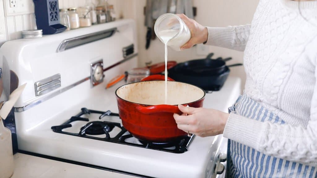 milk being poured into a red Dutch Oven