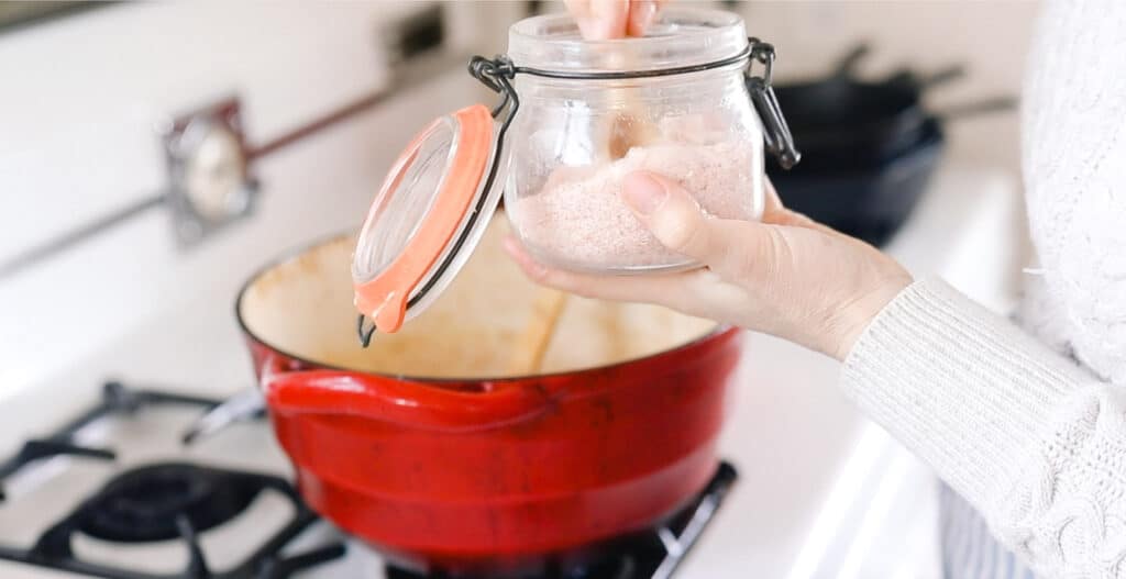 women adding salt into a large red Dutch Oven