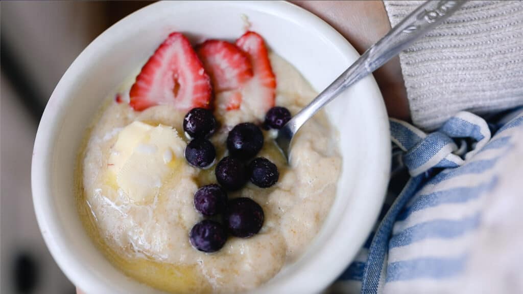 white bowl of einkorn breakfast porridge with strawberries and blueberries with a spoon