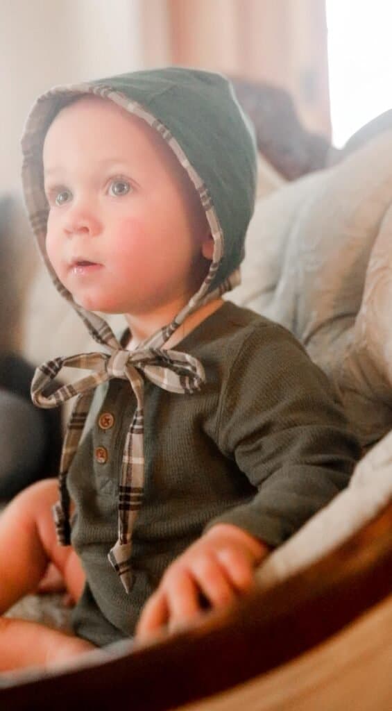 boy wearing a green long-sleeved onesie with a baby bonnet on