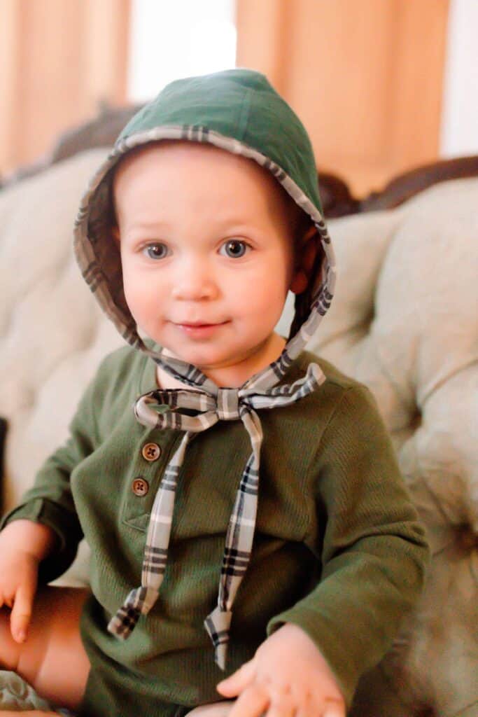 Baby boy in a green shirt wearing a green and plaid homemade bonnet