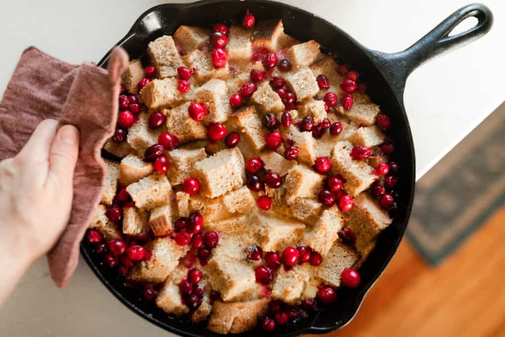 overhead photo of a cast iron skillet with baked French toast casserole with cranberries on top.