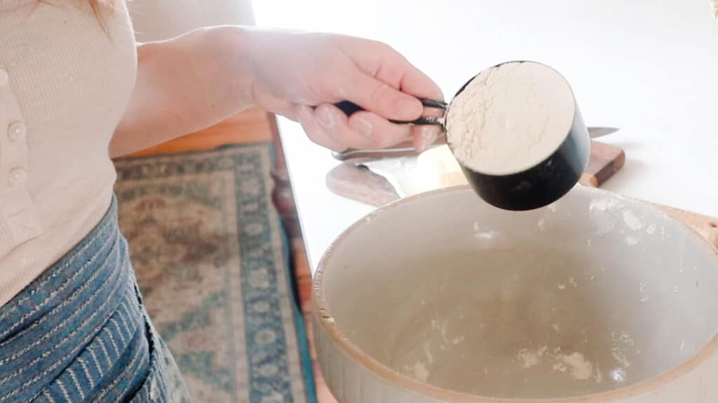 women wearing an apron pouring flour into a large bowl
