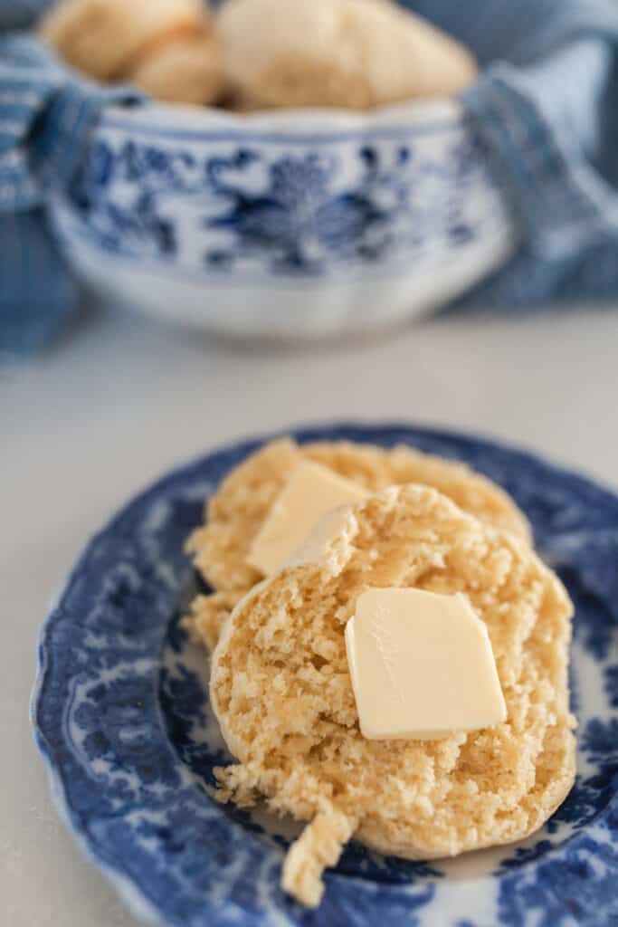 einkorn biscuits with a pat of butter on a antique blue and white plate with a bowl of more biscuits in the background