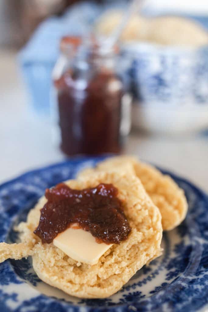 einkorn biscuits covered in butter and jam on a blue and white antique plate with jam and a bowl of biscuits in the background