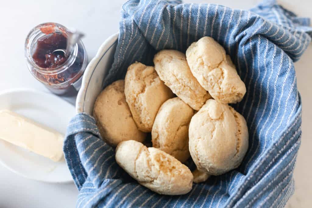 einkorn biscuits in a bowl lined with a blue and white stripped towel with jam and butter to the left