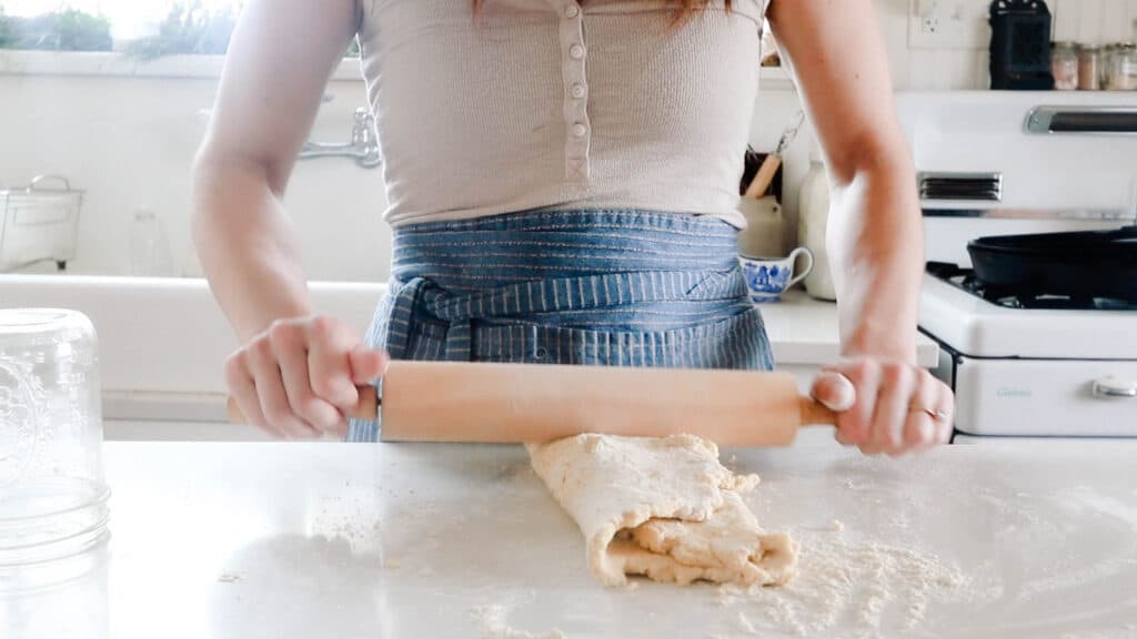 women rolling out einkorn biscuit dough on a white quarts countertop