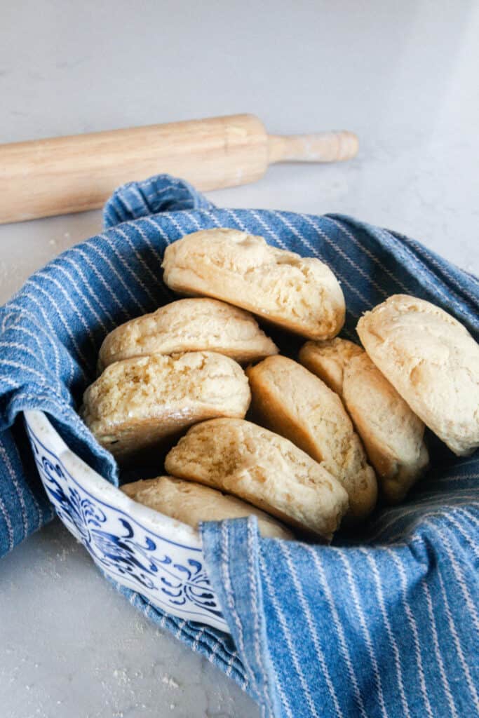 einkorn biscuits in a antique bowl lined with a blue and white stripped towel and a rolling pin in the background