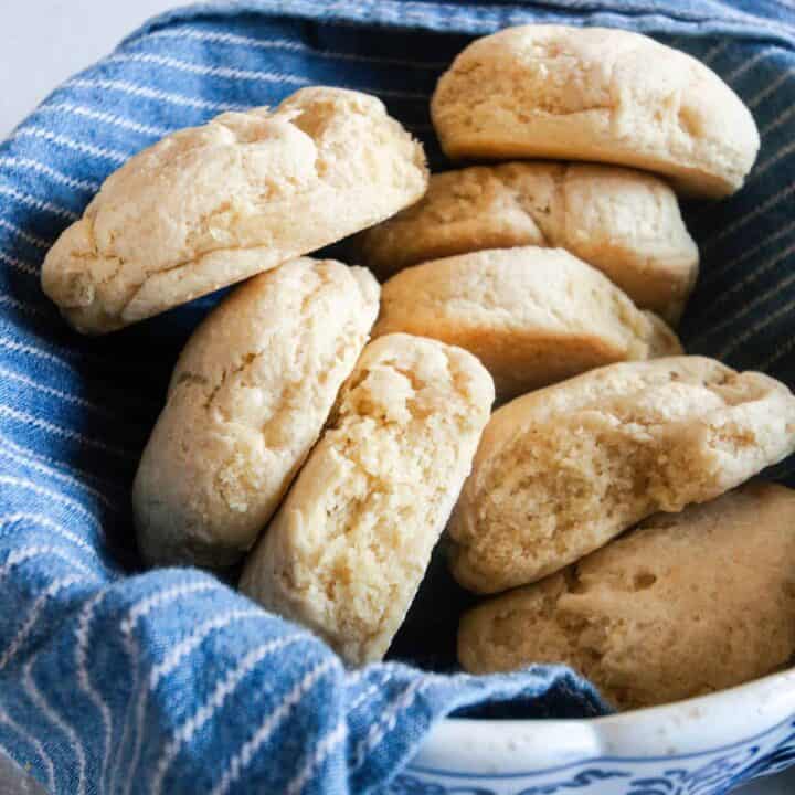 einkorn biscuits in a bowl lined with a blue and white stripped towel and a rolling pin in the background