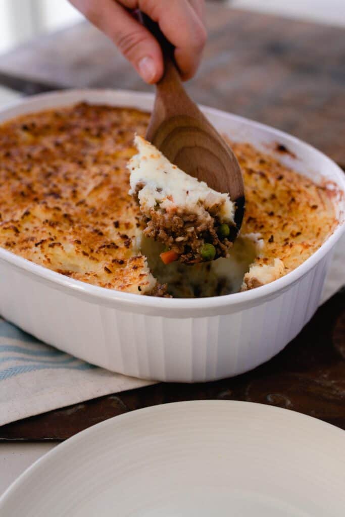 wooden spoon scooping out a baking dish of shepherd pie