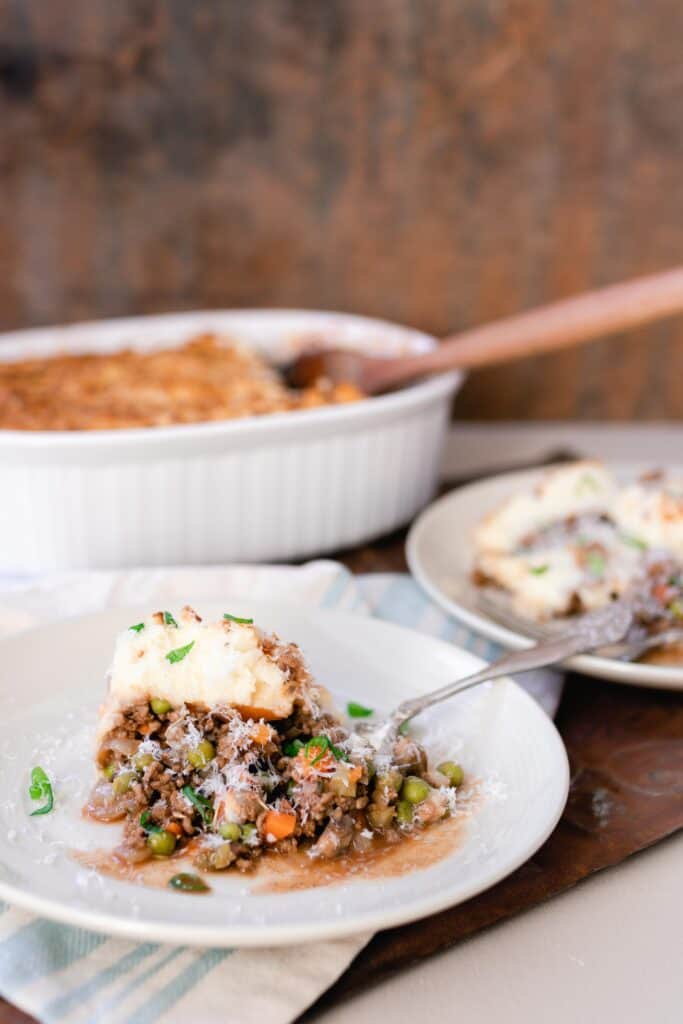 Shepherds pie on a white plate with a baking dish in the background