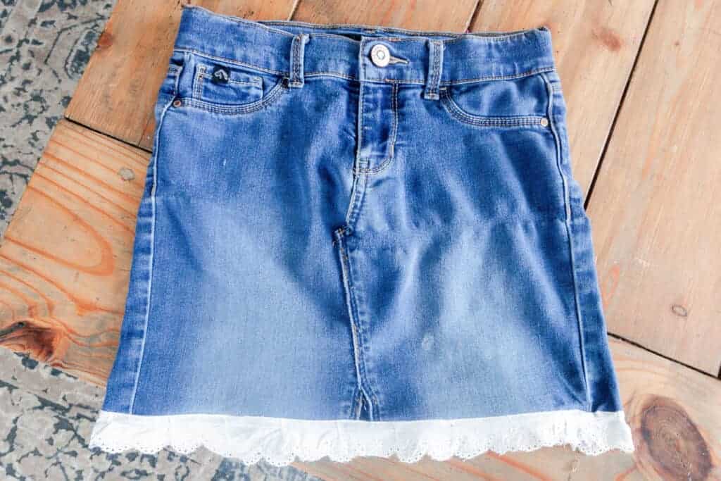 denim jeans turned into a skirt with a white eyelet trim laying flat on a wood table