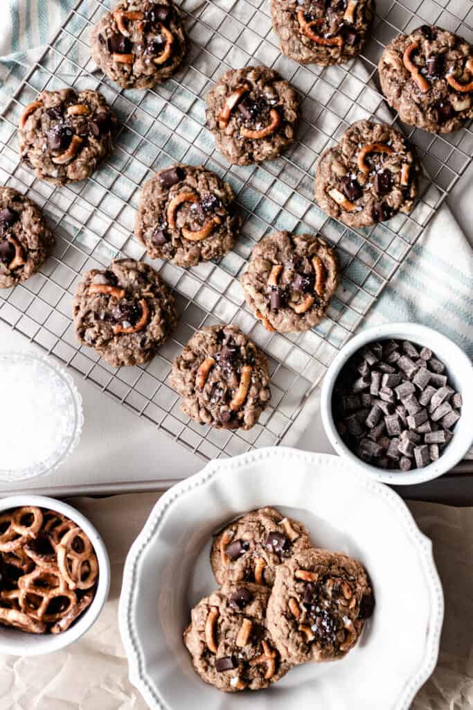 overhead photo lactation cookies on a cooling wrack. A plate of cookies sits right in front of the cooling rack and two containers of chocolate chunk and pretzels.