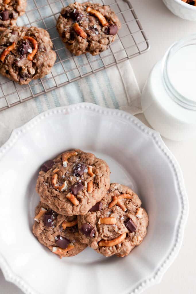 three oatmeal lactation cookies on a white plate with a cooling rack of more cookies behind it