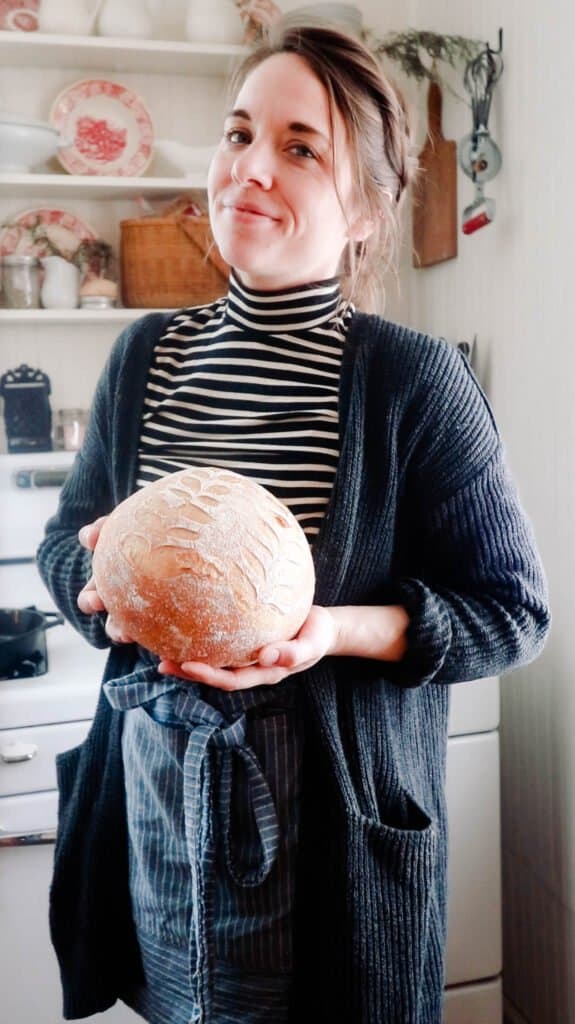 women wearing a black sweater holding a loaf of no-knead sourdough bread in a white kitchen