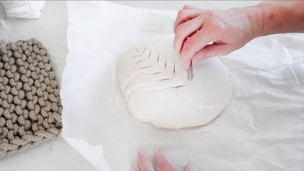 hand slicing sourdough bread dough with a lame to create a beautiful design