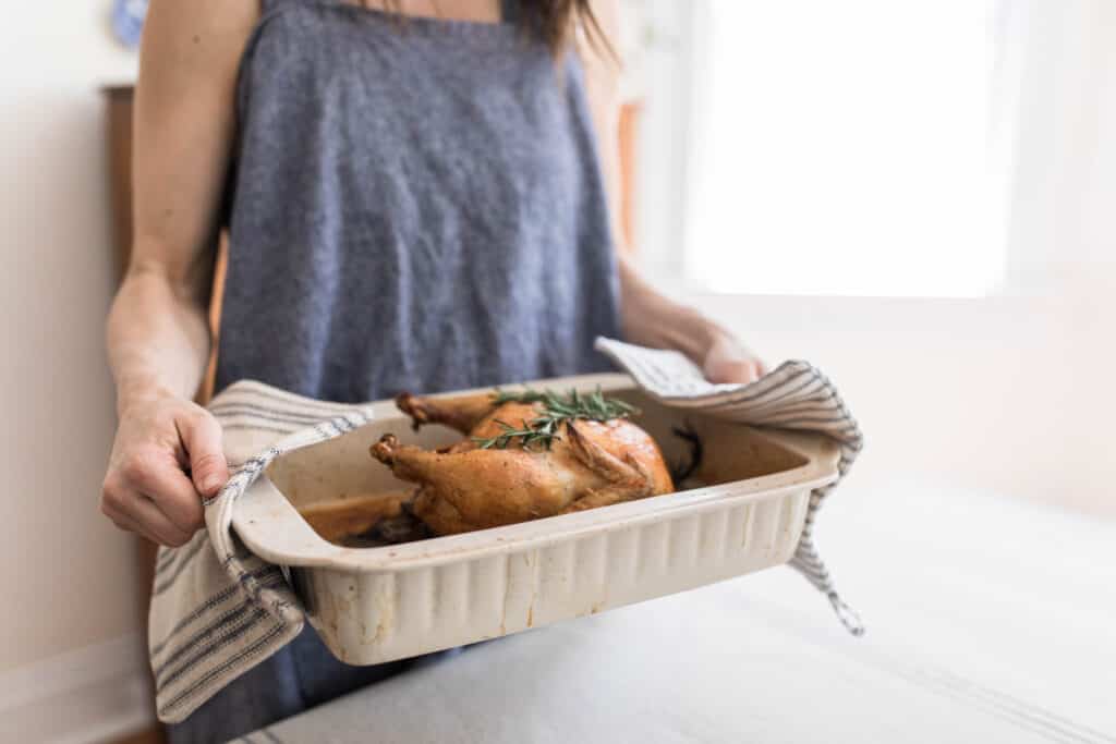 women using diy pot holders to hold a cream bakeware with a roasted chicken in it