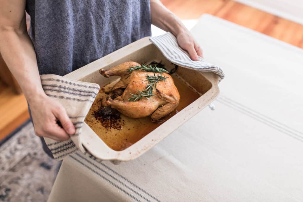 women using diy pot holders to carry a baking dish with a chicken covered in herbs