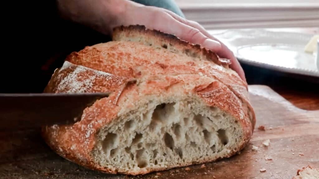 slicing a crusty loaf of bread on a wood cutting board