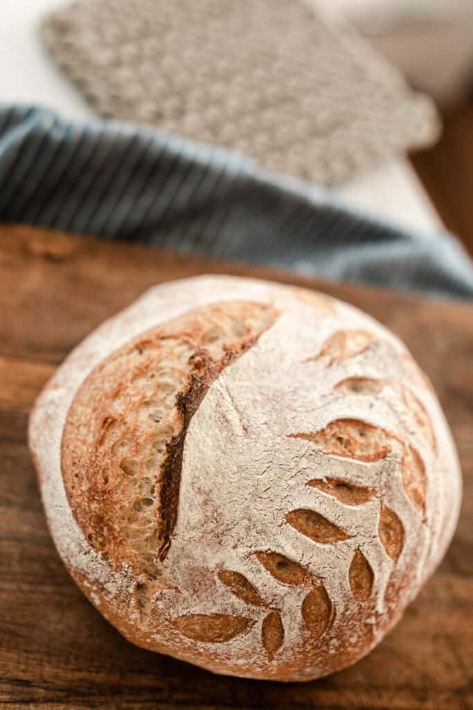 loaf of bread on a wood cutting board with a blue towel and crocheted in the background