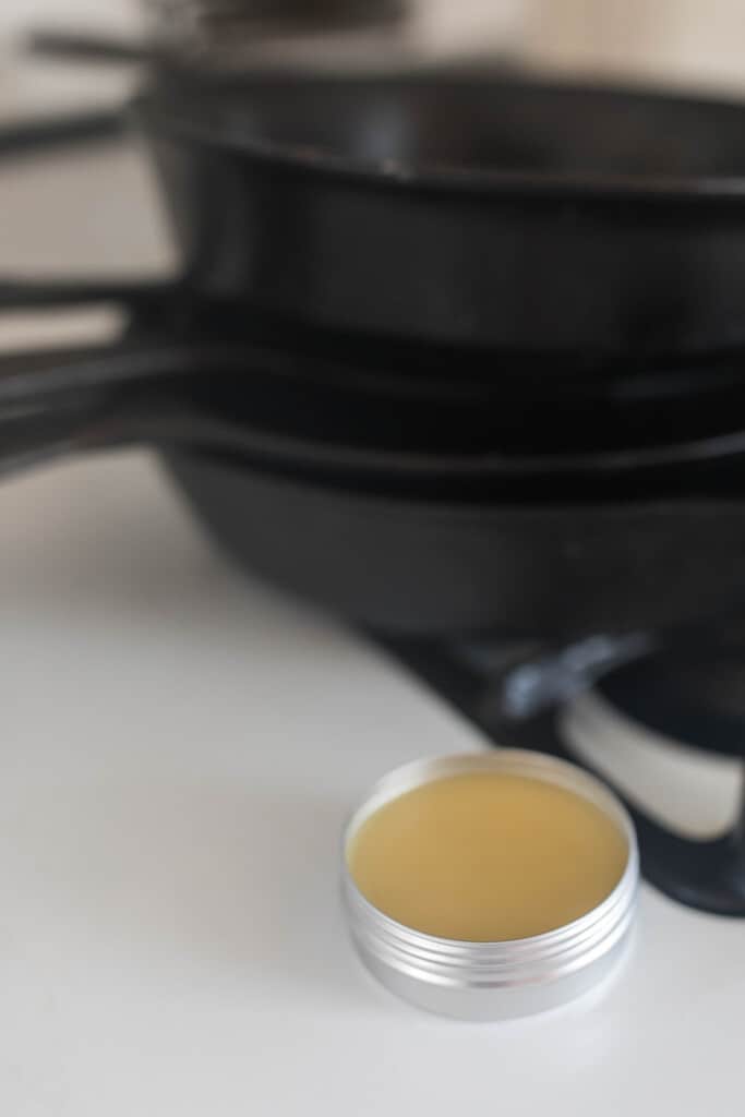 oil seasoning blend in a tin next to cast iron skillet stacked on a stove top