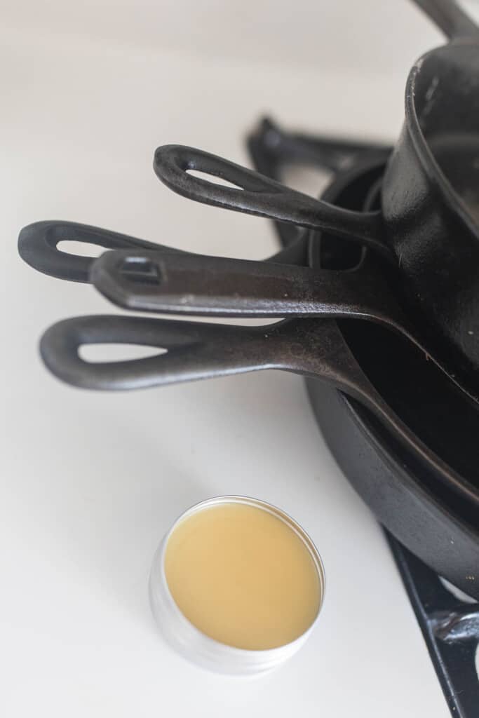 DIy cast iron seasoning oil in a tin next to cast iron skillets stacked on a stove