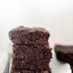 four einkorn brownies stacked on a white plate with a fork