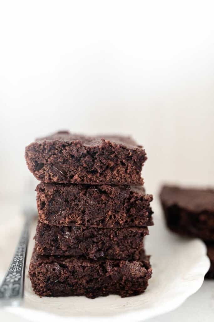 four einkorn brownies stacked on a white plate with a fork