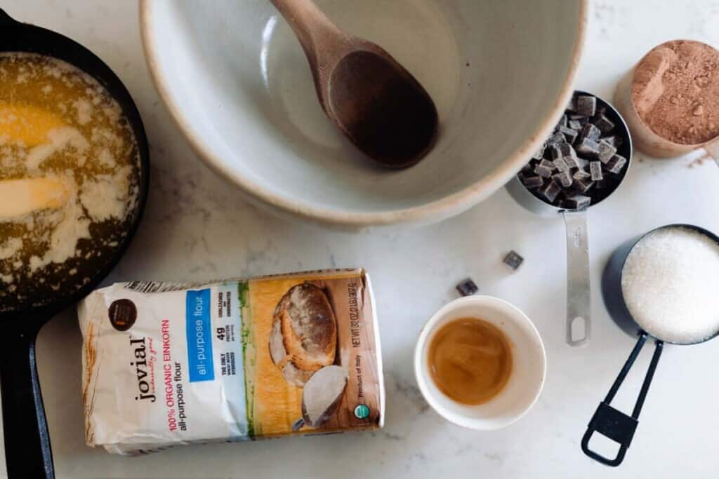 einkorn brownie ingredients around a large white bowl with a wooden spoon inside.