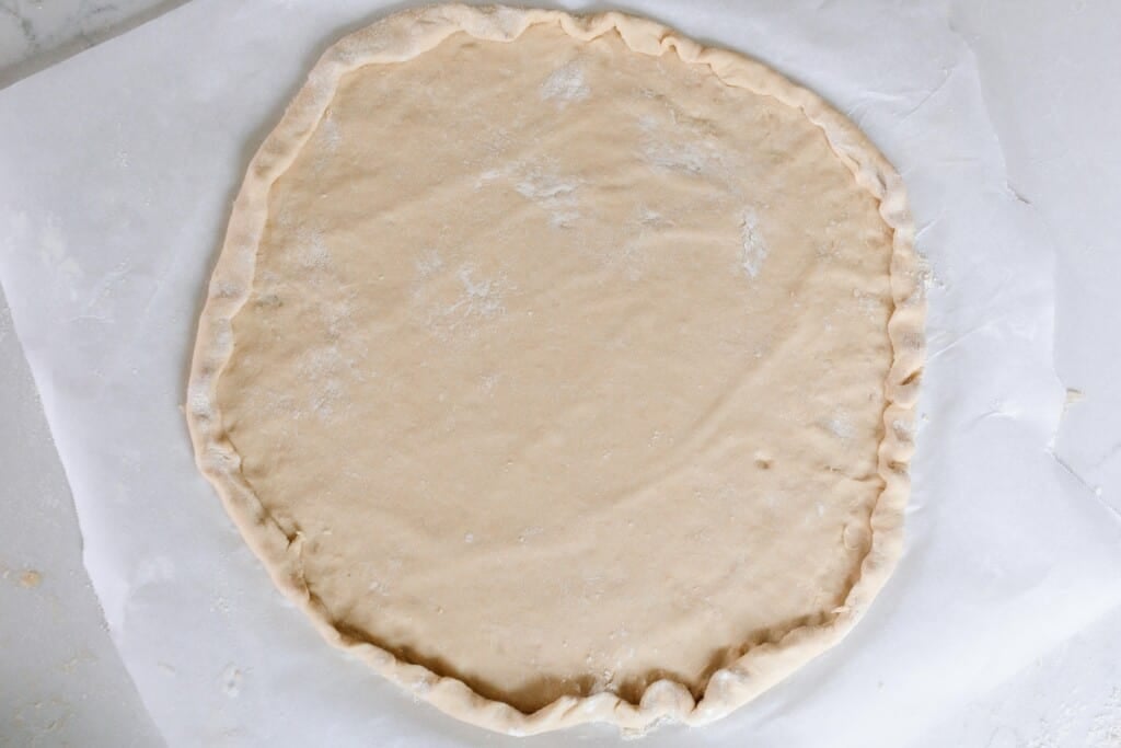 einkorn pizza dough rolled out in a circle with the edges turned over to make a thicker crust.