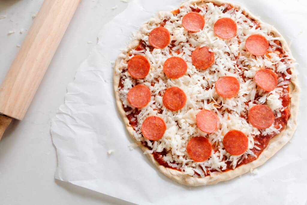 overhead photo of a pepperoni pizza on homemade pizza crust made from einkorn flour on parchment paper ready to go into the oven