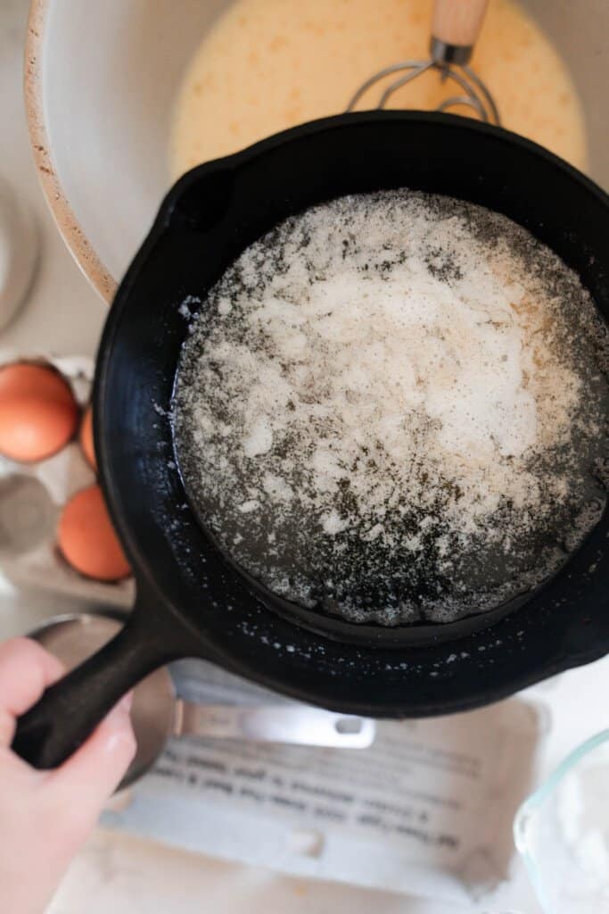 melted butter in a fast iron skillet about to be poured over a bowl of einkorn dutch baby batter