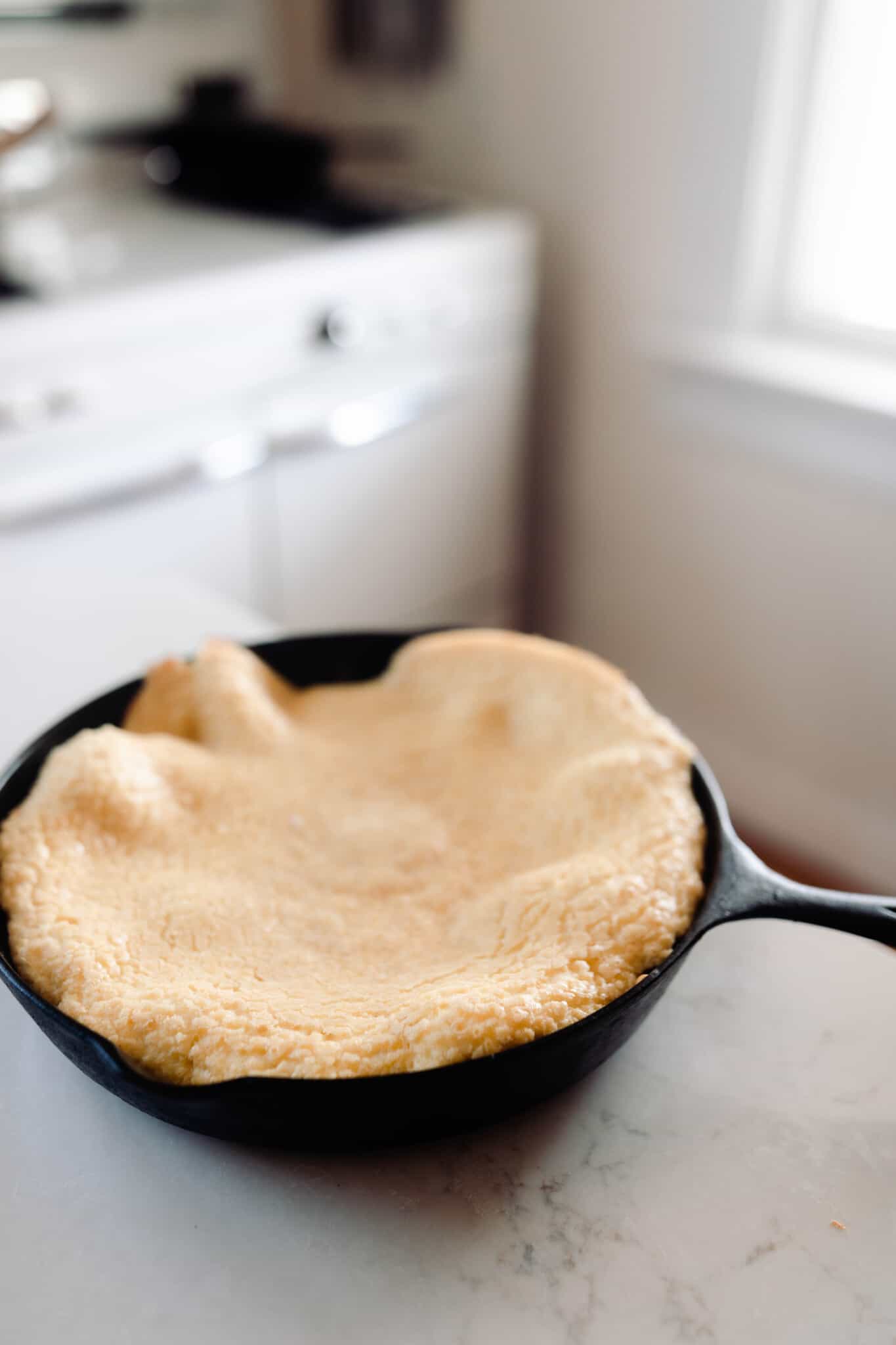 Einkorn puff pancake in a cast iron skillet on a countertop in a vintage inspired white kitchen.