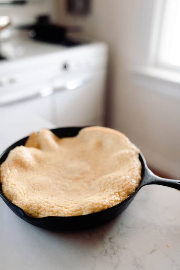 einkorn puff pancake in a cast iron skillet on a countertop in a vintage inspired white kitchen