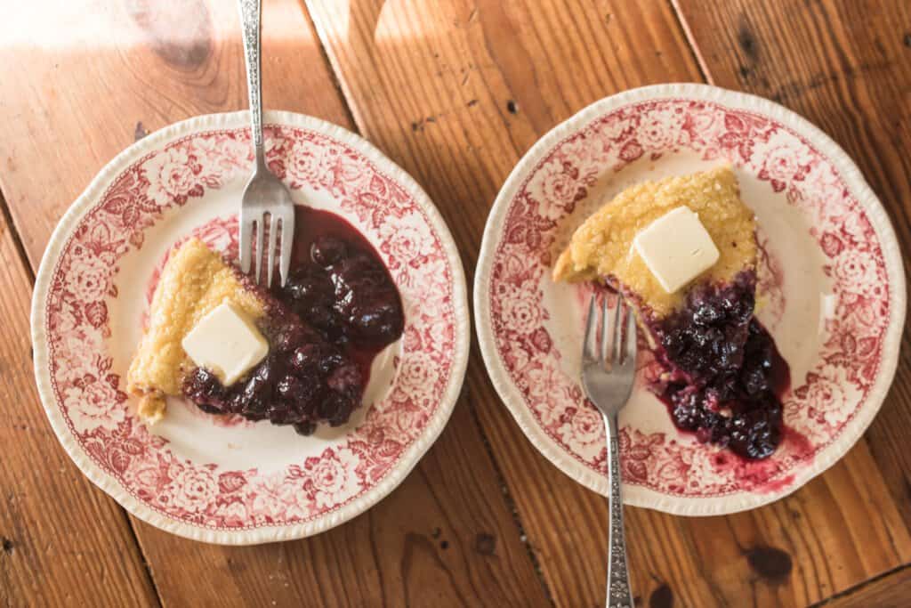 two red and white vintage plate with einkorn German pancakes, a pat of butter, and berry syrup