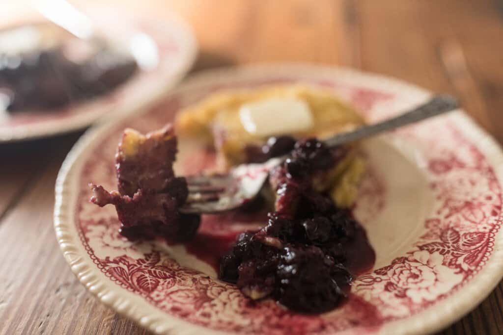 two red and cream vintage plates with einkorn dutch baby pancakes with berry syrup with a fork