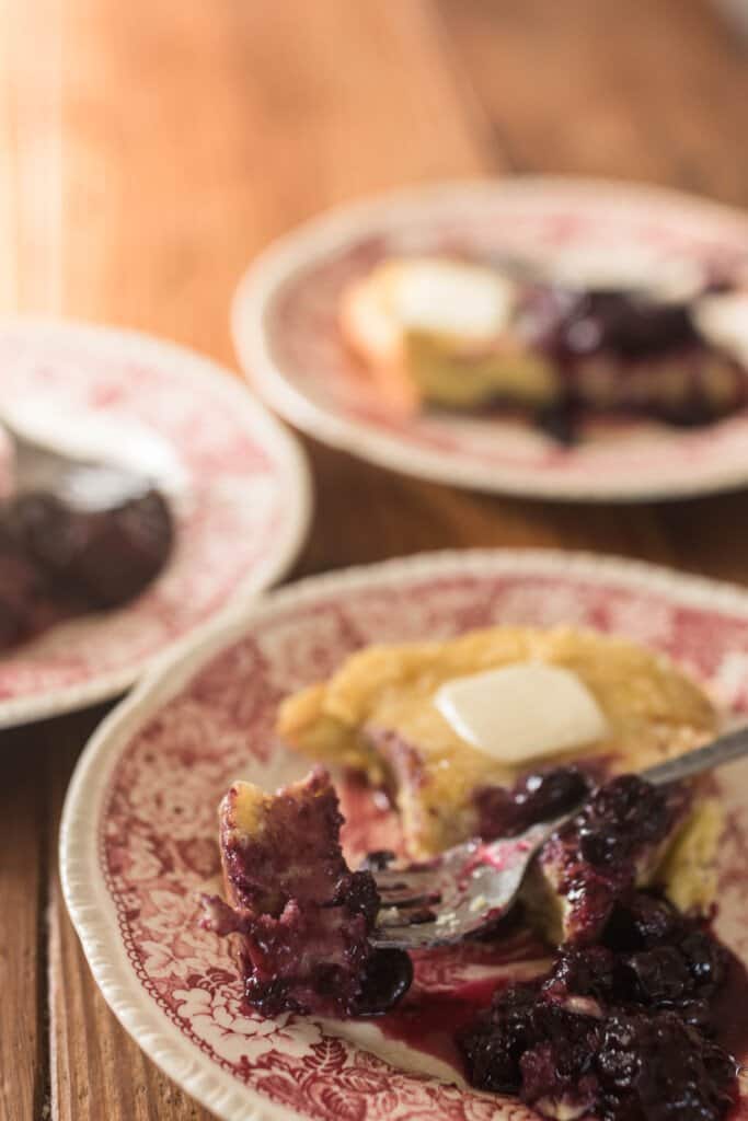 three plates of einkorn dutch baby pancakes with berry syrup on a wooden table