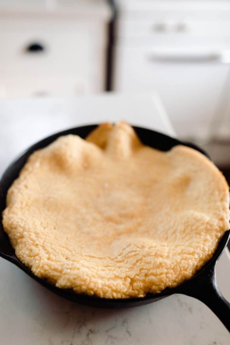 einkorn puff pancake in a cast iron skillet on white quarts countertop. A antique stove is in the background