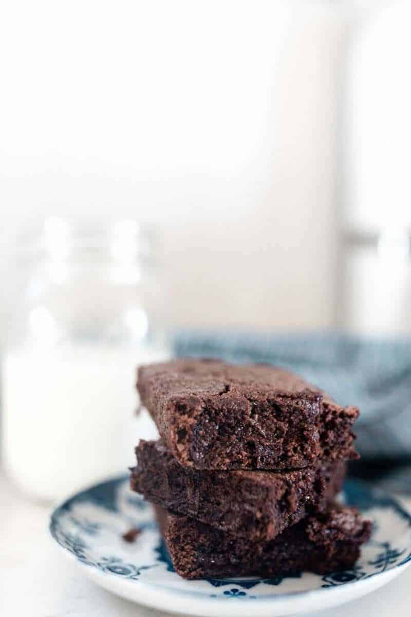 3 einkorn brownies stacked up on a blue and white plate with a glass of milk in the background