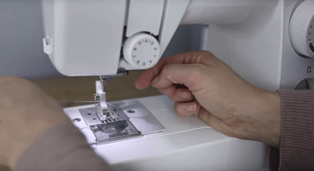 hand putting thread through the needle of a sewing machine