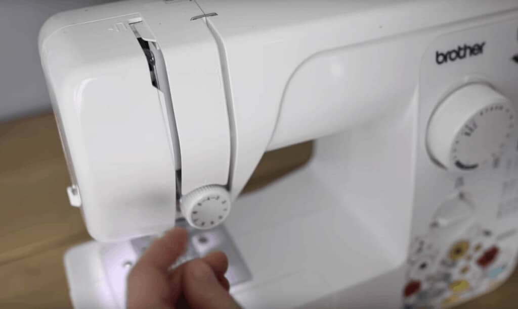 hand pulling the thread around the tension knob to thread a sewing machine