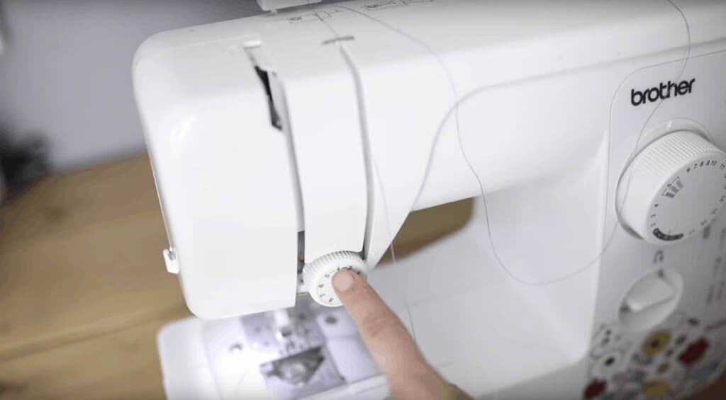 hand pointing to the tension knob on a sewing machine