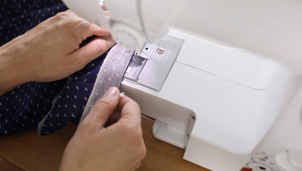 women using a sewing machine to create a hem with blue fabric with polkadots.